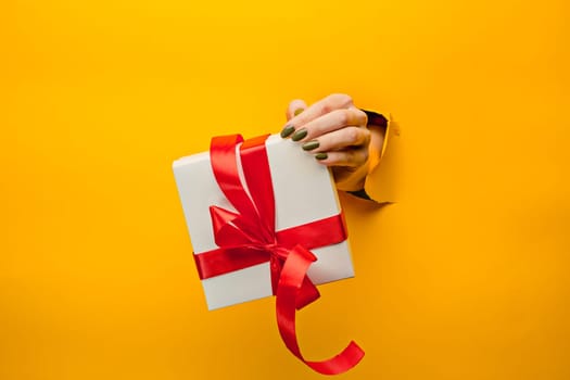 The close-up of female hand holding a present through a torn yellow paper, isolated