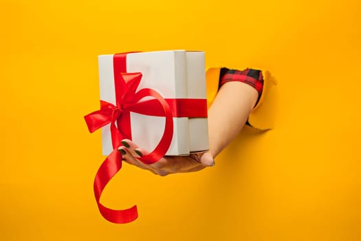 The close-up of female hand holding a present through a torn yellow paper, isolated
