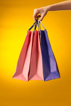 Female hand holding bright shopping bags on yellow