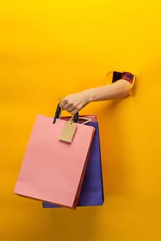 Female hand holding bright shopping bags on yellow