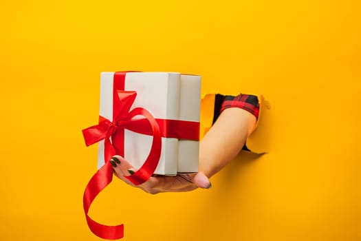 The close-up of female hand holding a present through a torn yellow paper, isolated
