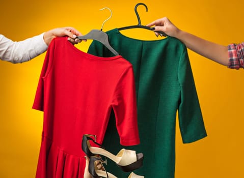 Textile, design, clothing, fashion concept. The female hands with dresses in her hands on yellow