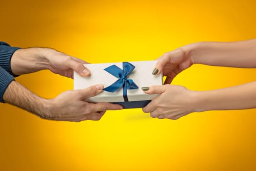 The closeup picture of man and woman's hands with gift box on yellow background