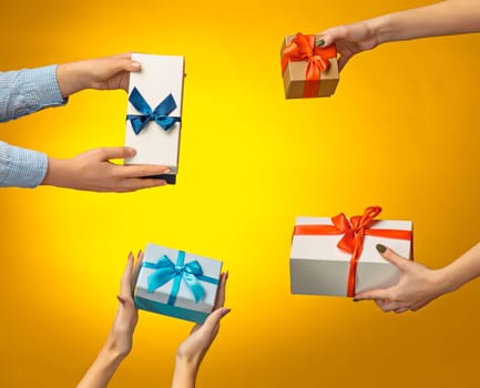 The closeup picture of man and woman's hands with gift box on yellow background