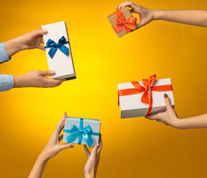 The closeup picture of man and woman's hands with gift box on yellow background