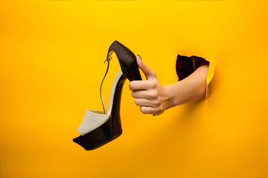 The female shoe on hand through a torn yellow paper
