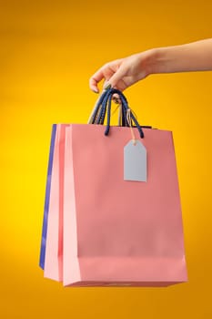 Female hand holding bright shopping bags on yellow