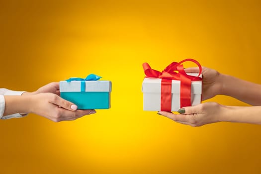 The closeup picture of man and woman's hands with gift box on yellow background