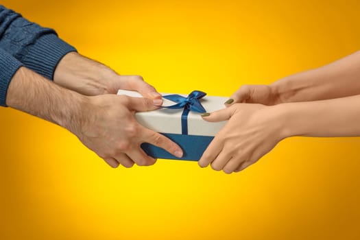 The closeup picture of man and woman's hands with gift box on yellow background