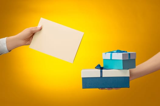 The closeup picture of man and woman's hands with gift box on yellow background with copy space on empty blank