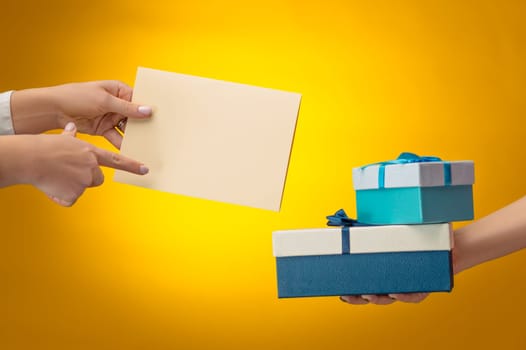 The closeup picture of man and woman's hands with gift box on yellow background with copy space on empty blank