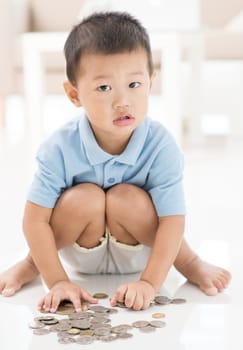 Asian preschool boy saving coins at home. Child education fund concept.