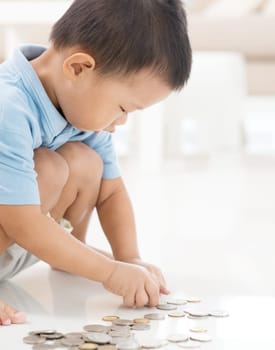 Asian kid saving coins at home. Child education fund concept.