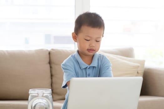 Asian boy using computer laptop at home. Child education and technology concept.