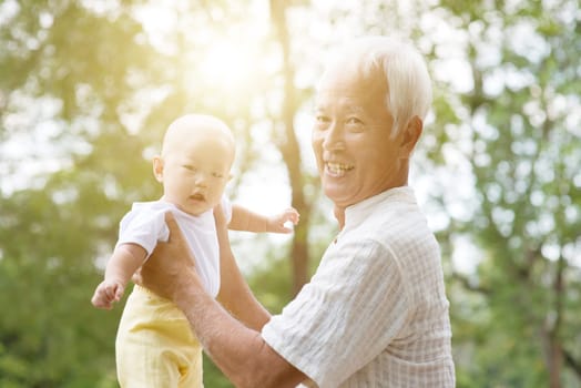 Grandfather holding baby grandson at outdoor park, Asian family, life insurance concept.