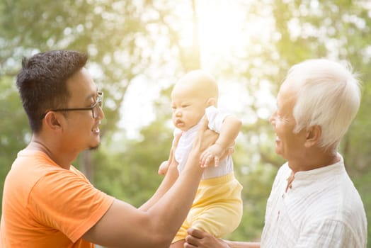Happy grandfather, father and baby grandchild at outdoors park. Asian multi generations family.