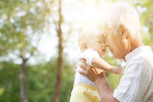 Grandfather kissing baby grandson at outdoor park, Asian family, life insurance concept.