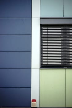 The modern façade of a modern residential building with a metal window with metal blind and a warning light.