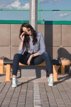 A beautiful girl with sunglasses and torn jeans and a striped shirt. Against the background of large steel structures. Artistic photography. beauty and fashion, style.