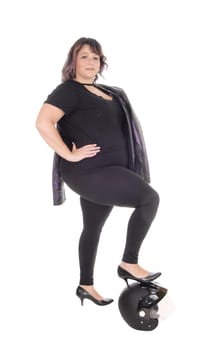 A lovely woman dressed in black standing with one leg on her motor.cycle helmet and jacket over shoulder, isolated for white background.