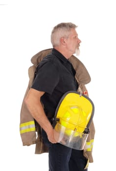 A middle age firefighter man standing in profile with his jacket over.his shoulder and helmet in his hand, isolated for white background.