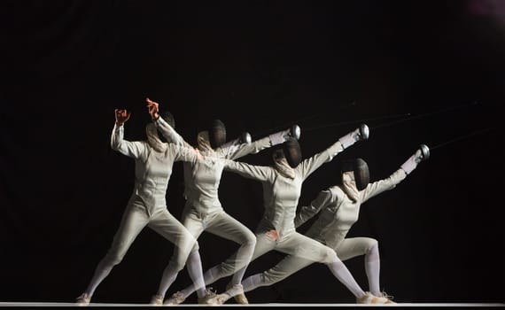Full-length portrait of woman wearing white fencing costume and black fencing mask practicing with the sword on black background