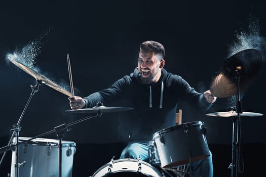 Drummer rehearsing on drums before rock concert. Man recording music on drum set in studio with show effect in the form of flour