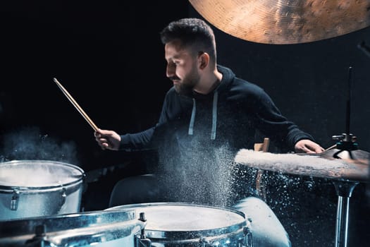 Drummer rehearsing on drums before rock concert. Man recording music on drum set in studio with show effect in the form of flour