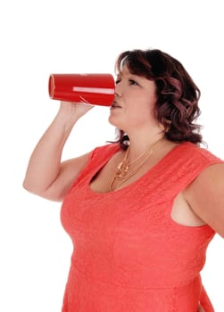 An overweight woman in a red dress standing in profile with a necklace.and drinking coffee from a red mug, isolated for white background.