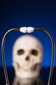 Stethoscope i focus and blurry skull isolated on black blue background