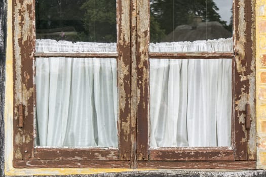 part of old vintage window with brown cracked paint and white retro curtains