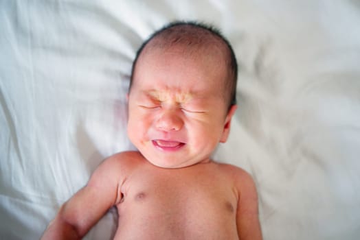 Asian newborn crying baby boy. 7 days old new born child tired and hungry in bed.
