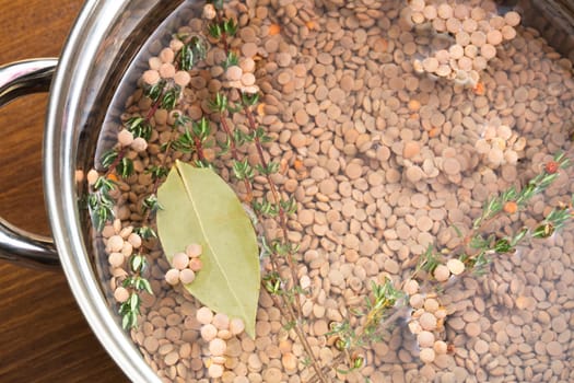 Lentils, thyme and bay leaf in pot with water, ready for cooking.