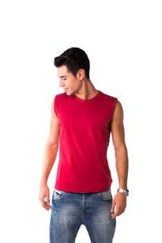 Attractive smiling young man in red sleeveless shirt and jeans, looking down at blank space next to him, isolated on white