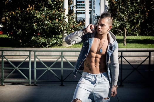 Handsome Athletic Man in Denim Fashion Outfit Showing Sexy Six Pack Abs Calling Through Mobile Phone Outdoor.