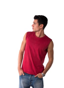 Attractive young man in red sleeveless shirt and jeans, looking to a side at blank space next to him, isolated on white