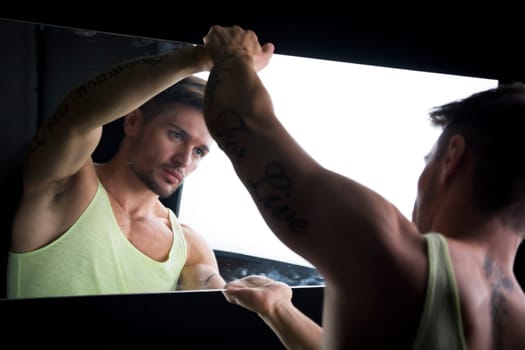 Narcissistic handsome young man leaning forwards admiring his reflection in the mirror in a show of self-absorption