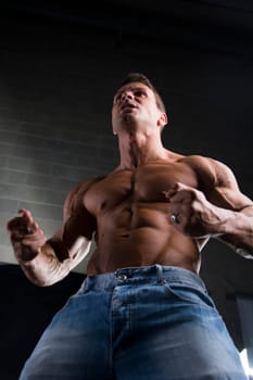 Low angle close up view of a strong young man with a muscular physique standing clenching his fists to emphasize his arm and shoulders muscles