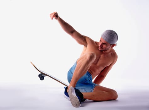Shirtless Man Sitting on Skateboard in Studio with White Background Posing as if in Mid Trick