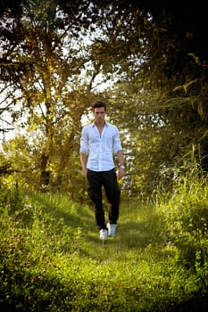 Handsome sexy man outdoors in the garden standing on fresh green grass amongst trees looking seductively at the camera