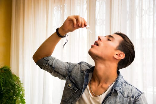 Head and Shoulders of Man Dropping Medicine from Eyedropper into Mouth from Hand Held Above