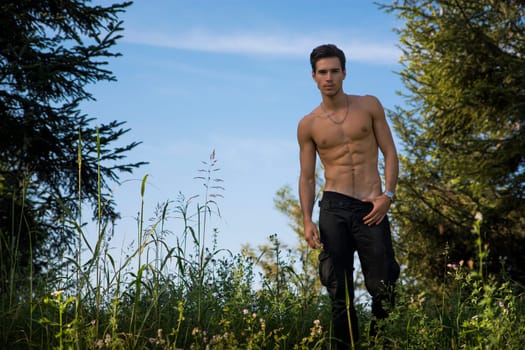 Gorgeous Young Shirtless Man with Sexy Abs, Strike a Pose at the Garden While Looking at the Camera.