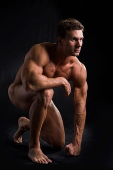 Totally Nude Young Muscle Man Crouching on one Knee in Studio with Black Background