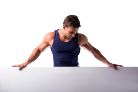 Strong muscular young man standing holding a blank horizontal white banner looking down at the copyspace for your text, on white