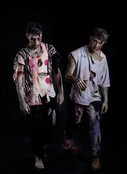 Two male zombies standing on black background walking towards camera