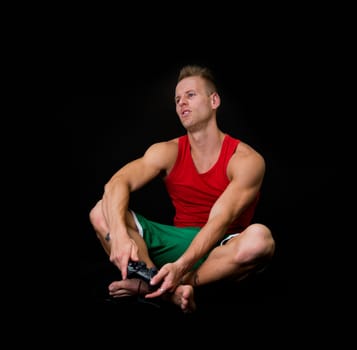 Young Muscled Man Sitting on Floor Holding Joystick with Disappointed Expression on Face. Isolated on Black.