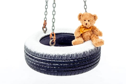 A stuffed bear sitting on snow covered tire swing.
