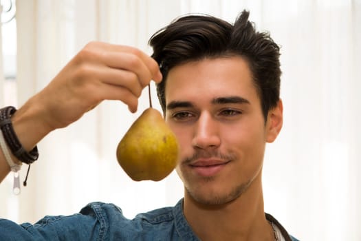 Young man holding and looking at a large delicious ripe yellow pear dangling from his hand