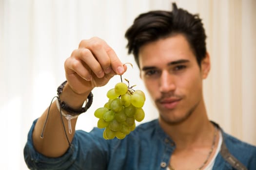 Young man holding a large delicious ripe bunch of grapes dangling from his hand, focus to the fruit