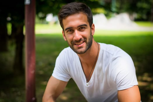 Handsome friendly young man outdoors in park smiling at camera